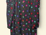 black polka dot dress hanging on a hanger against a white wall