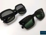 une paire de lunettes de soleil noires aux verres verts, posée sur une surface blanche