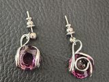 a pair of pink and silver earrings on a black leather surface