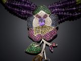 a close up of a necklace with a purple flower and green leaves