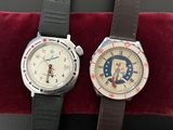 two wrist watches sitting on a red velvet cushion