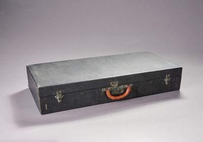 une valise noire munie d'une poignée rouge, posée sur une surface blanche