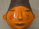 un vase orange orné d'un visage en bois