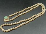 un collier de perles blanches orné d'une perle en verre verte et d'un fermoir doré