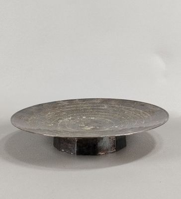 une assiette en argent posée sur un socle noir, sur une surface blanche