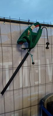 une pancarte fixée sur le mur d'un immeuble, à laquelle est accrochée une tondeuse à gazon verte