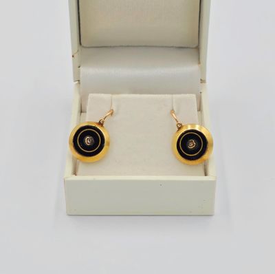 une paire de boucles d'oreilles noires et dorées dans un écrin sur fond blanc