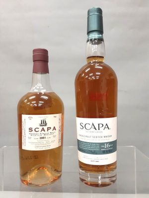 Deux bouteilles de Scappa et une bouteille de vin sont posées sur une étagère transparente.