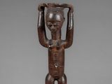 a wooden statue of a man holding a basket on his head