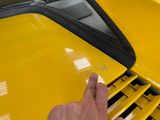 someone is pointing at the side of a yellow car with a black hood