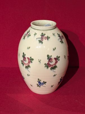 a white vase with flowers on it sitting on a red surface