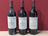 three bottles of red wine sit on a table in front of a red wall
