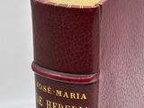 an old book with a red cover sitting on top of a white table