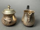 two silver pots with faces on them sitting next to each other