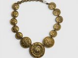 un collier en or composé de pièces suspendues à une chaîne, sur fond blanc