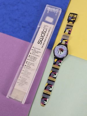 a watch sitting on a colorful surface next to a tube of glue