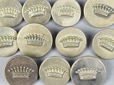 six silver buttons with crowns on them sitting on a white surface