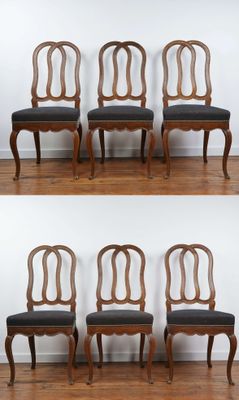 four chairs with black upholstered seats are lined up against a white wall