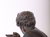 statue of a man sitting on a stool with his hands on his knees