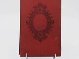 an old red book sitting on top of a metal stand