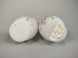 two white cups with gold designs on them on a gray surface