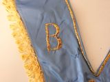 a close up of a blue and gold dress with a monogram on it