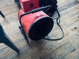 un ventilateur rouge posé par terre à côté d'un sac noir