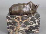 statue of a rhino lying on a rock with a coin in its mouth
