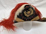 un chapeau noir orné de plumes rouges, posé sur une surface blanche