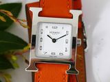 a small square watch with a silver face on a orange strap