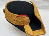 a black hat with a gold band and a red button
