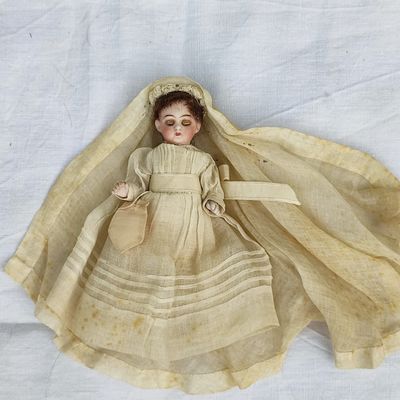 une vieille poupée allongée sur un drap blanc avec un voile sur la tête