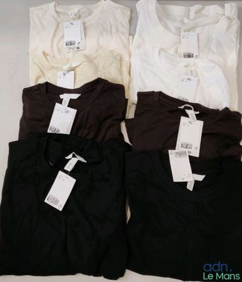 Trois t-shirts sont posés sur une surface blanche, avec leurs étiquettes encore attachées.