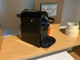a black coffee maker on a wooden shelf next to a roll of tape