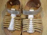 pair of toddler ' s gold sandals on a wooden floor