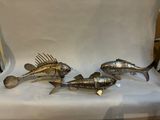 trois poissons en métal posés sur une table blanche, à côté d'une chaise
