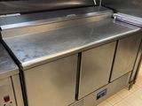 un grand plan de travail en inox dans une cuisine où des couteaux sont accrochés au mur