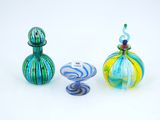 trois vases en verre de couleurs différentes posés l'un à côté de l'autre sur une surface blanche