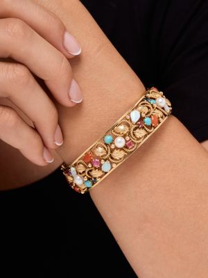 a close up of a woman ' s arm wearing a gold bracelet with multi colored stones