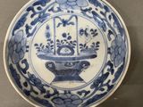 a blue and white plate with a basket of flowers on it