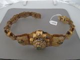 gold bracelet with green stones on display on a table