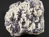 un gros plan sur un morceau de roche présentant des cristaux blancs et violets sur fond noir