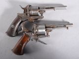deux vieux revolvers posés l'un sur l'autre sur une surface blanche