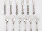 six fourchettes et six couteaux en métal argenté sont disposés sur une surface blanche