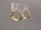 une paire de boucles d'oreilles créoles dorées et argentées posées sur un présentoir en acrylique transparent