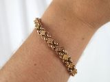 someone is holding a gold bracelet with a flower design on it