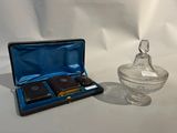 un récipient en verre contenant un flacon de parfum, à côté d'un récipient en verre contenant du parfum