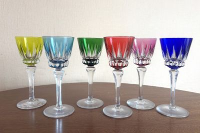 six verres à vin alignés sur une table, avec un mur blanc en arrière-plan