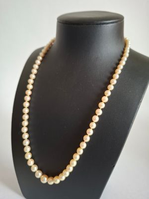 a white pearl necklace on a black mannequin with a gold clasp