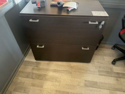a desk with a file cabinet and a chair in the corner